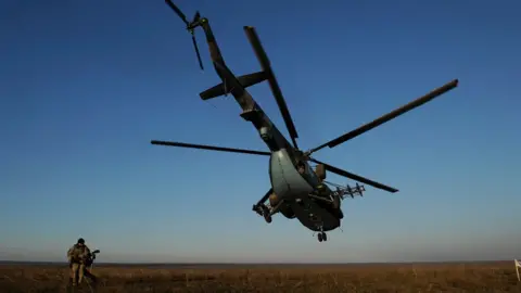 AFP A serviceman walks near a Ukrainian military helicopter flying during military drills on an open green space with blue skies