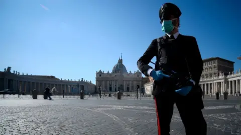 Getty Images An armed police officer, wearing a face mask, patrols a closed and deserted St Peter's Square in the Vatican