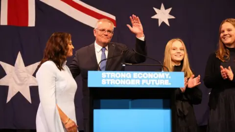 Getty Images Scott Morrison waves behind a lectern beside his family