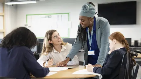 Getty Images Female students working on assignment with help from black teacher