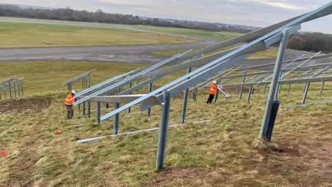 Moulton College Mounting frame for solar panels standing on grass, with two students in orange hi-viz working on it