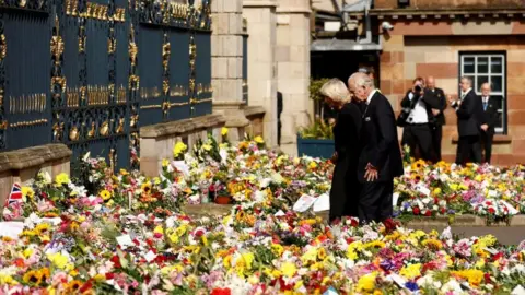 Reuters King Charles and Camilla look at the thousands of floral tributes left at the gates of Hillsborough Castle in honour of Queen Elizabeth II