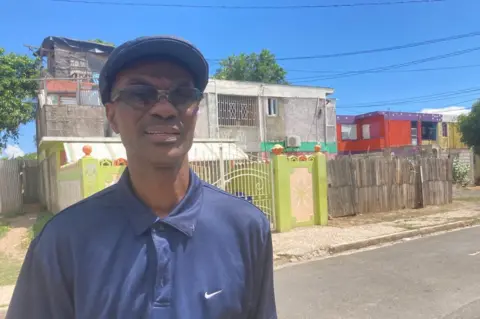 Dr Howard Harvey stands in front of a colourful lime green fence in Trench Town