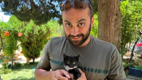 Reuters visuals journalist Issam Abdallah holds a kitten while posing for a picture in Saaideh, Lebanon