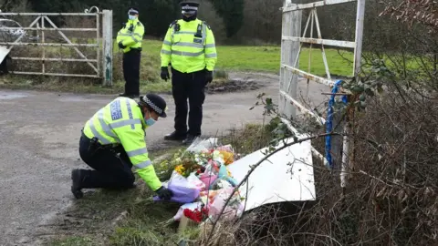 PA Media A police officer lays flowers left by members of the public