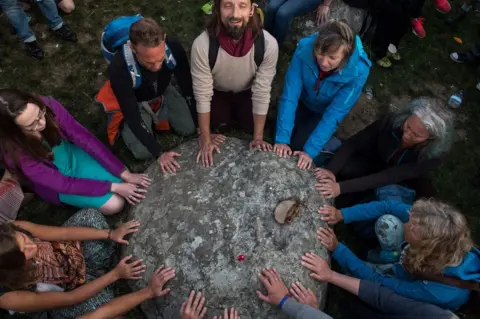 CHRIS J RATCLIFFE / Getty Images Revellers in a circle touch a stone at Stonehenge