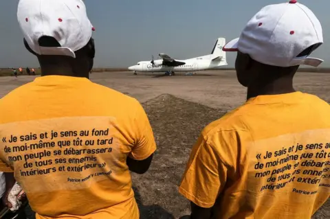 AFP An excerpt from the last letter to his wife written in captivity by slain Congolese independence leader Patrice Lumumba is seen printed on T-shirts worn by members of the public in Tshumbe, Democratic Republic of Congo, on 22 June, as the airplane carrying Lumumba's family lands.