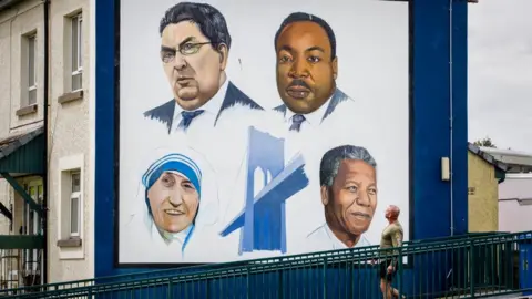 PA Media A man walks past the Bogside mural in Derry City of John Hume, Martin Luther King Jr, Mother Teresa, and Nelson Mandela