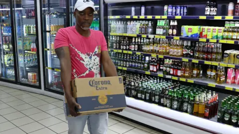 Reuters A shopper carries a box of alcohol with the words "Corona extra" ahead of a nationwide lockdown for 21 days to try to contain coronavirus in Johannesburg, South Africa