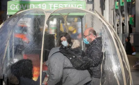 Reuters People take Covid-19 tests at a pop-up testing site in New York on 1 December. They are wearing masks and can be seen inside a transparent tent