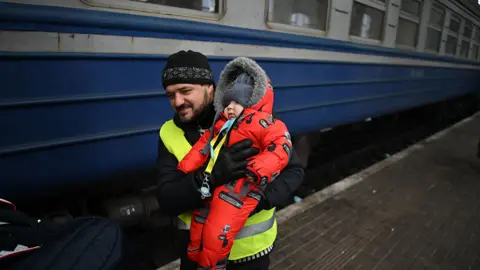 Getty Images A volunteer holds a baby to help him to get on board to a train which prepares to depart from a station in Lviv, western Ukraine, enroute to Poland, on March 3, 2022