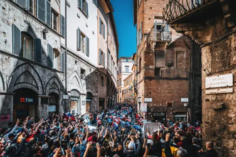 Ashley & Jered Gruber The peloton rides through Siena, Italy, at the start of stage 12 of the 2021 Giro d'Italia