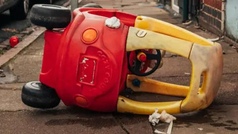 @khandiephoto Yellow and red "little tikes" car on its side on a pavement