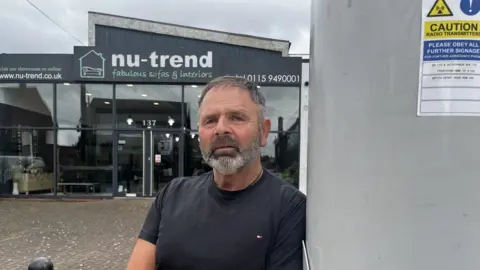 BBC Business owner Mr McGrath next to the pole outside his shop