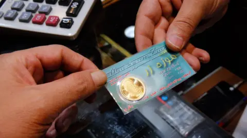 EPA An Iranian shopkeeper sells a gold coin at a shop in Tehran (5 August 2018)