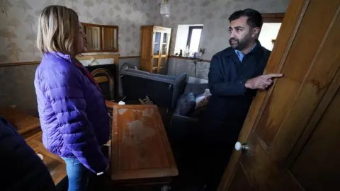 PA Media First Minister Humza Yousaf (right) speaks to Paul Fowlie and partner Kim Clark as he looks at water damage in their house during a visit to Brechin, Scotland