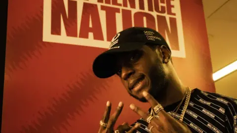 Ben Dance The rapper 6lack stands in front of a signt that says 'Apprentice Nation'