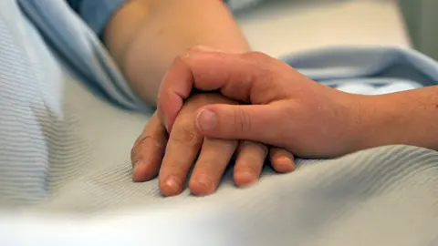 BBC A hospital patient's hand is held by the hand of another person