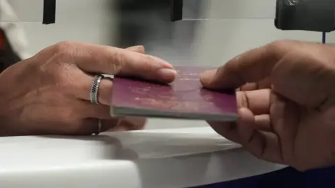 BBC A passport being passed across adesk