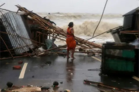 Reuters A woman stands next to her stall damaged by heavy winds at a shore ahead of Cyclone Yaas in Bichitrapur in Balasore district in the eastern state of Odisha India, May 26, 2021.