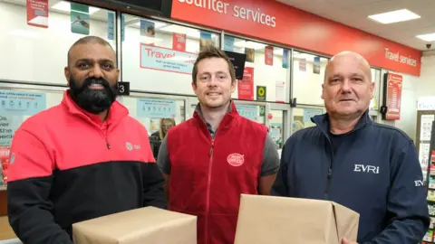 DPD, Post Office and Evri staff standing in a post office holding parcels.