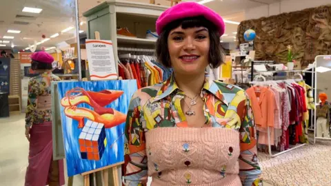 A woman with a bob in a pink beret standing in a clothes shop