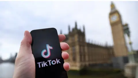 EPA-EFE/REX/Shutterstock Person holding a device with the Tiktok logo outside Parliament