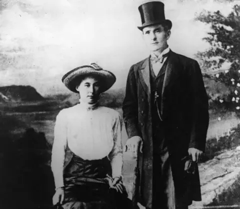 Getty Images The 'Brides in the Bath' murderer George Joseph Smith (1872 - 1915) standing in front of a painted backdrop of the countryside with the first of his murder victims, Beatrice Mundy,