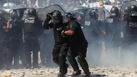 Reuters A police officer assists a colleague during clashes with demonstrators as lawmakers debate a pension reform measure, in Buenos Aires