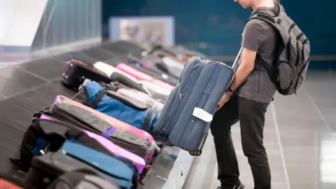 Getty Images Traveller lifting suitcase from luggage carousel at an airport