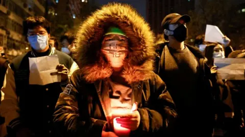 A person holds a candle, as people gather for a vigil and hold white sheets of paper