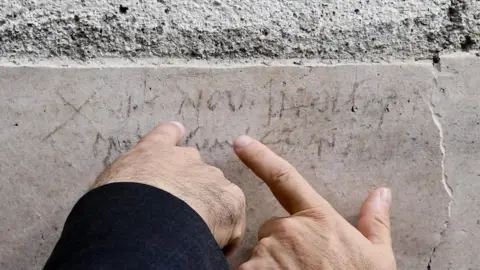 EPA Two men's' hands point to a faded inscription on the stonework of a wall. While mostly incomprehensible to those who do not read ancient Latin, the letters NOV can clearly be seen - a reference to November