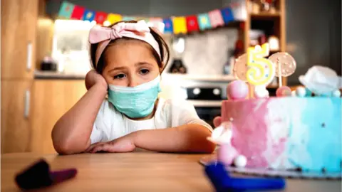 Getty Images Child with birthday cake and face covering