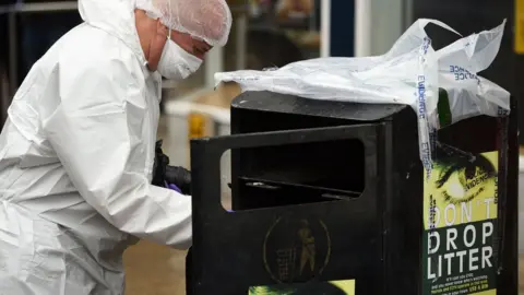 Getty Images Police forensics officer searching a bin