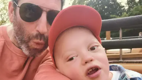 Team Sebastian Sebastian Nunney - young boy wearing a cap and being held by his father