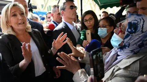 Getty Images French far-right party Rassemblement National (RN) presidential candidate Marine Le Pen (L) gestures as she speaks with a woman during a campaign visit at Pertuis market on 15 April