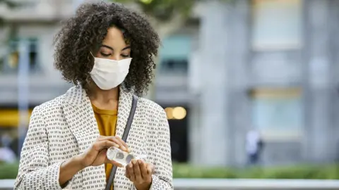 Getty Images Woman wearing mask with hand sanitizer