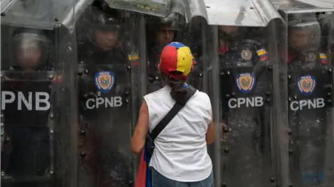 An anti-Maduro demonstrator waves a Venezuelan flag in front of the Venezuelan National Police officers during a demonstration against the government of Nicolas Maduro organized by supporters of Juan Guaido on March 10, 2020 in Caracas,