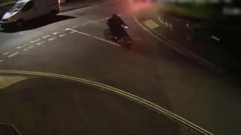 CCTV of a person on a bike, driving down a dark main road