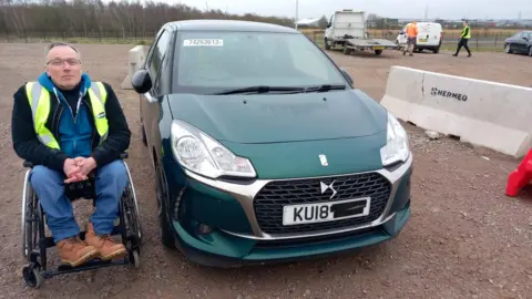 Andrew Miller Andrew Miller beside his old car at a salvage yard