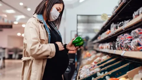 Getty Images Woman shopping for food wearing face mask