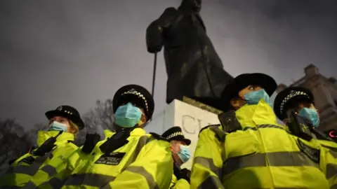 Getty Images A group of Met Police officers dressed in reflective jackets and wearing Covid face masks stand in front of a statue of Winston Churchill with a cloudy night sky in the background