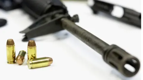 Getty Images Four bullets beside the barrel of a rifle resting on a table