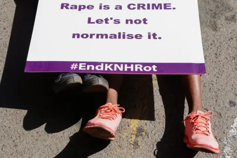 EPA Women from different organizations hold placards and lie on the ground during a protest against Kenya"s biggest referral hospital Kenyatta National Hospital (KNH) after allegations of sexual harassment on women within the hospital"s maternity wing in Nairobi, Kenya, 23 January 2018.