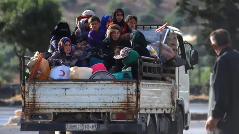 AFP Displaced Syrians sit in the back of a lorry as they flee along the M4 highway, in Ariha, Idlib province (8 June 2020)