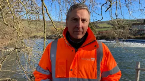 Andy Mears standing next to the River Avon in a Wessex Water hi-vis jacket