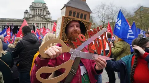 Niall Carson/PA Man holding scissors with sign saying 'no more cuts'