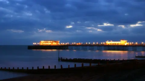 Getty Images The illuminated pier glows against a cloudy evening sky