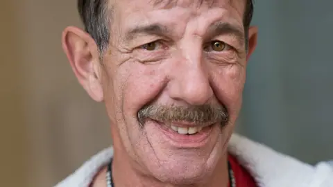 Huntingdon Academy Picture of Ian Coates. He is a 65-year-old man with a moustache who is smiling in this picture