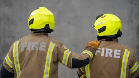 PA Media Two firemen face a wall in their uniform